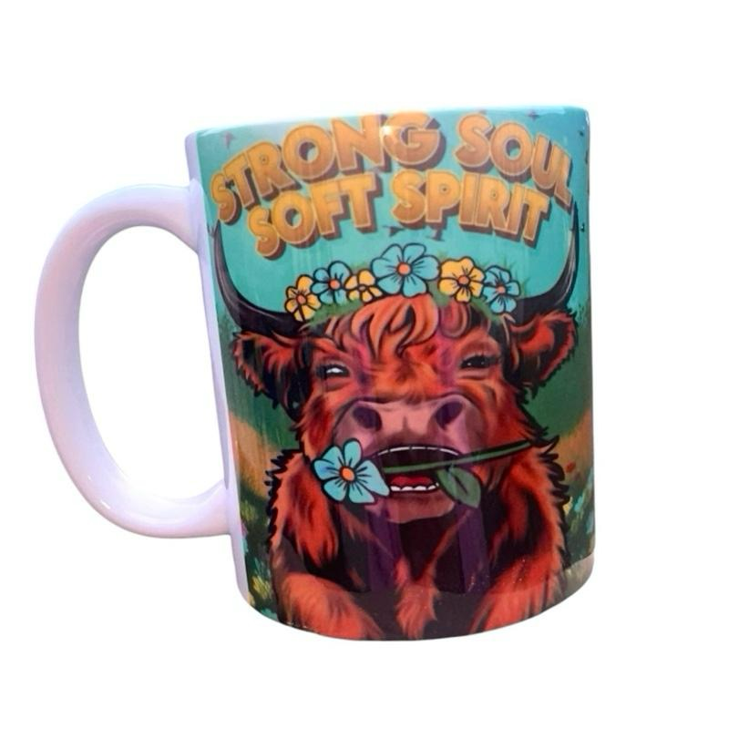 ASKMOLSHighland cow with floral crown and blue flower in mouth, text Strong Soul Soft Spirit on teal background.